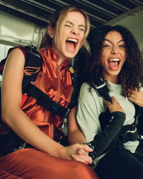 Cena do filme: as duas amigas rindo dentro do avião, de equipamento de paraquedismo, antes do salto